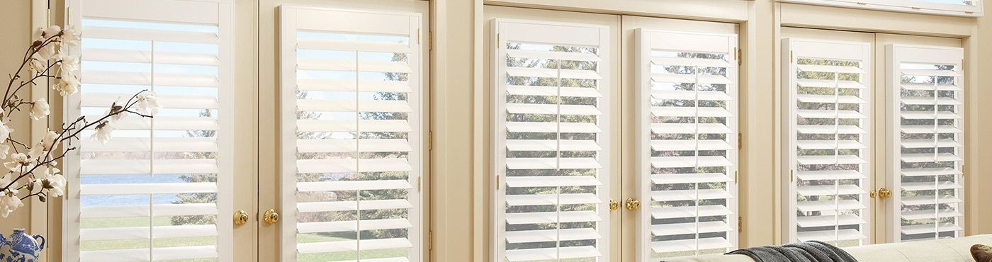 A row of white shutters on a window in a room.