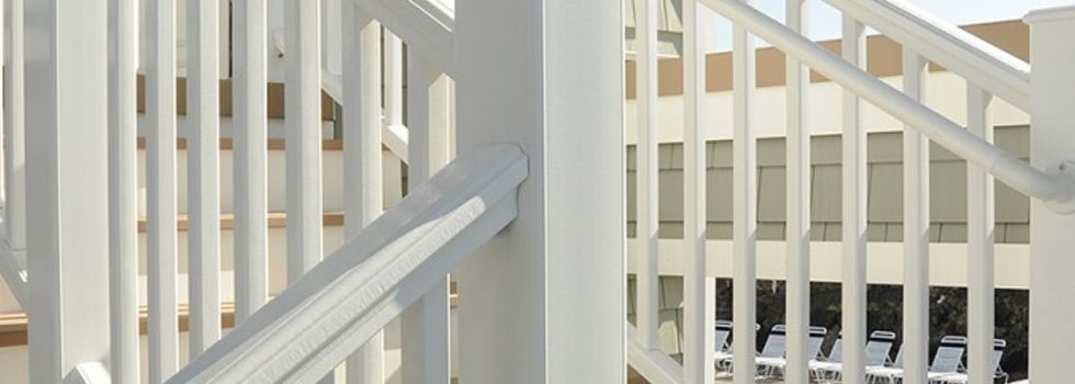 A close up of a white railing on a staircase with a building in the background.