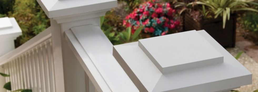 A close up of a white railing with flowers in the background.