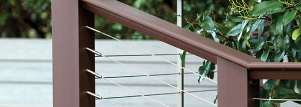 A close up of a wooden railing with stainless steel wire.