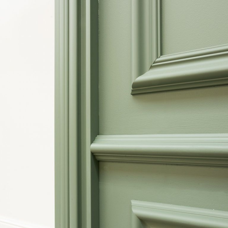 Close-up of a section of a green painted door with detailed molding and trim, next to a white wall.