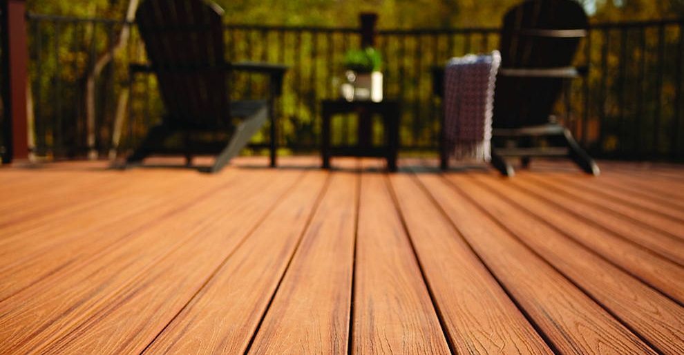 Wooden deck with Adirondack chairs and small table on a balcony, overlooking trees.