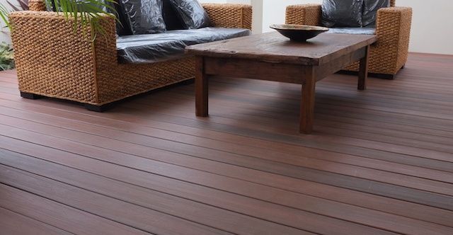 Wicker sofa and coffee table on a wooden deck, interior setting. Dark wooden floor and brown furniture.