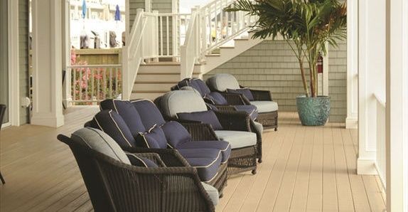Outdoor seating area with blue cushioned wicker furniture on a wooden deck, with stairs and a large potted palm tree in the background.