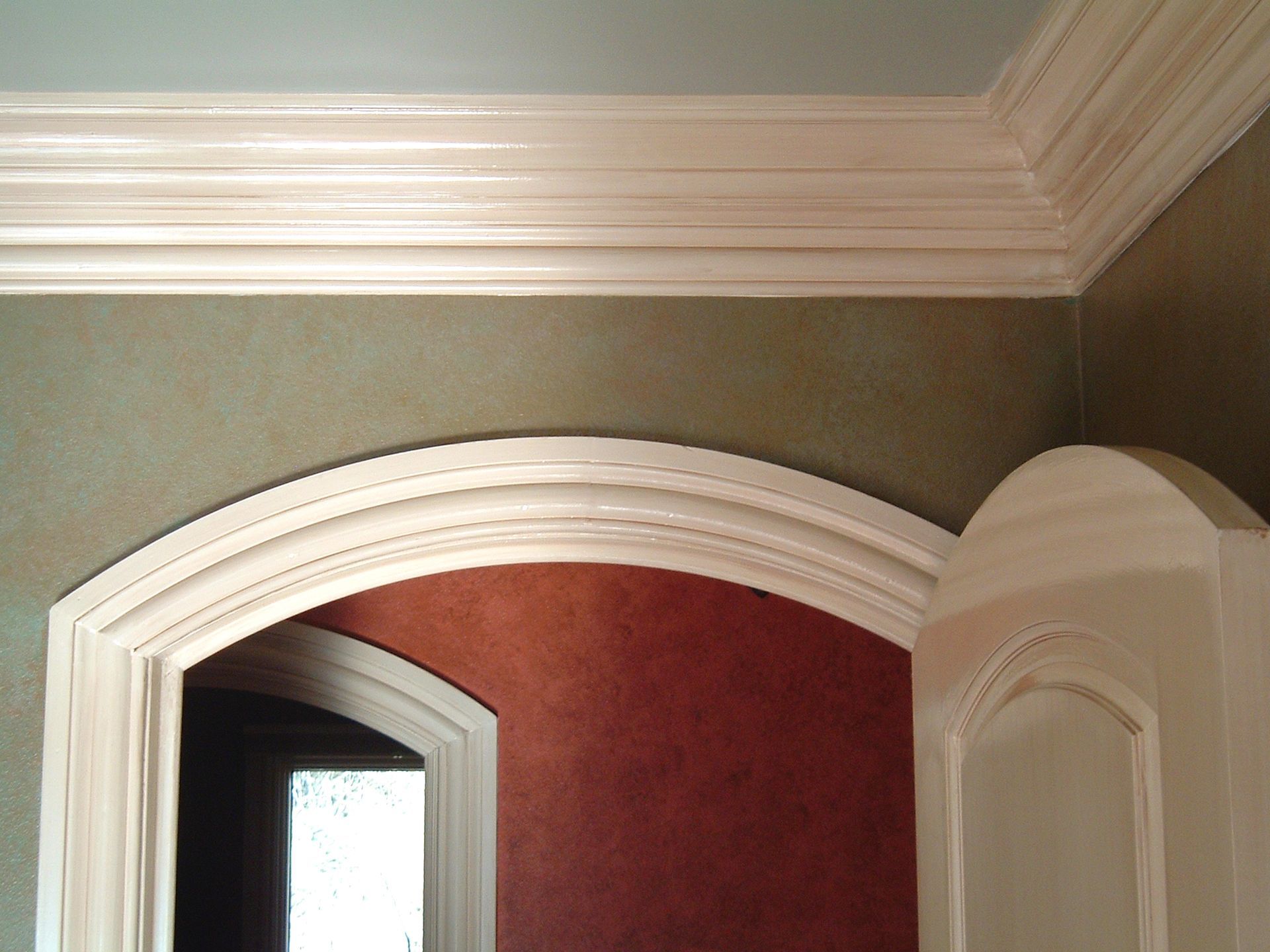 White molding frames an arched doorway and the top of the walls painted with olive and red hues.