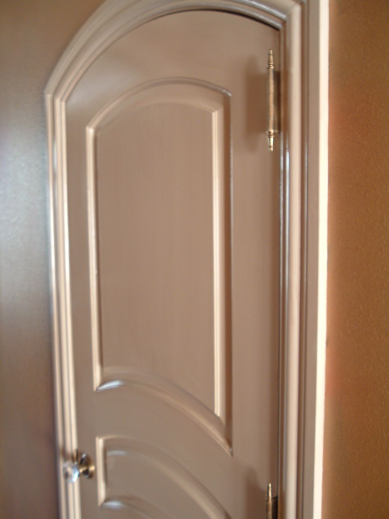 White arched-top interior door with gold hinges and a doorknob, set in a white frame.