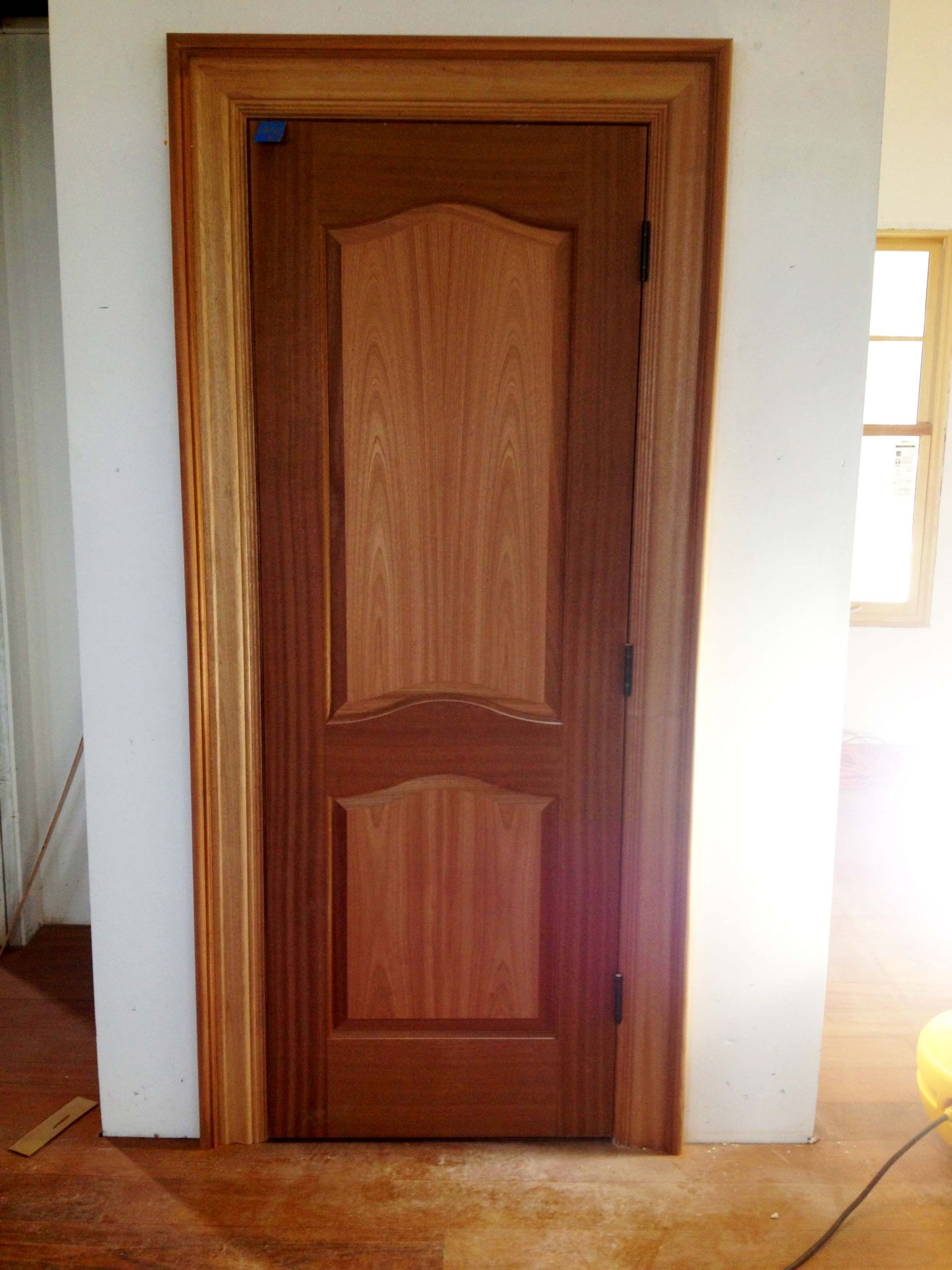 Wooden door with a light brown finish set in a door frame against a white wall.