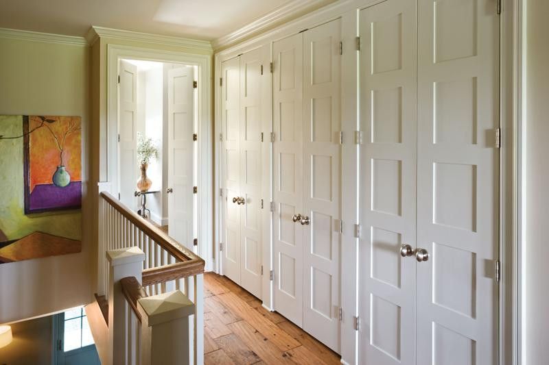 Hallway with white paneled doors, a light-colored wooden floor, and a staircase with a wood railing. A painting hangs on the left wall.