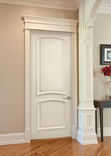 White interior door with decorative trim, beside a column, on a light wood floor.