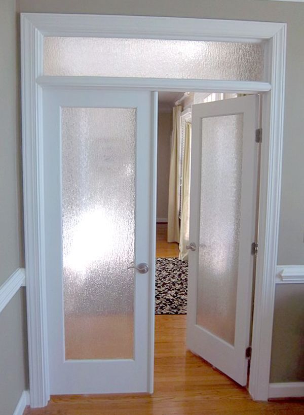 White French doors with textured glass, one open, leading into a room with hardwood floors and a patterned rug.