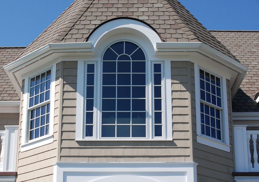 A three-sided house turret with tan siding and multiple white-framed windows. The central window has a rounded top.