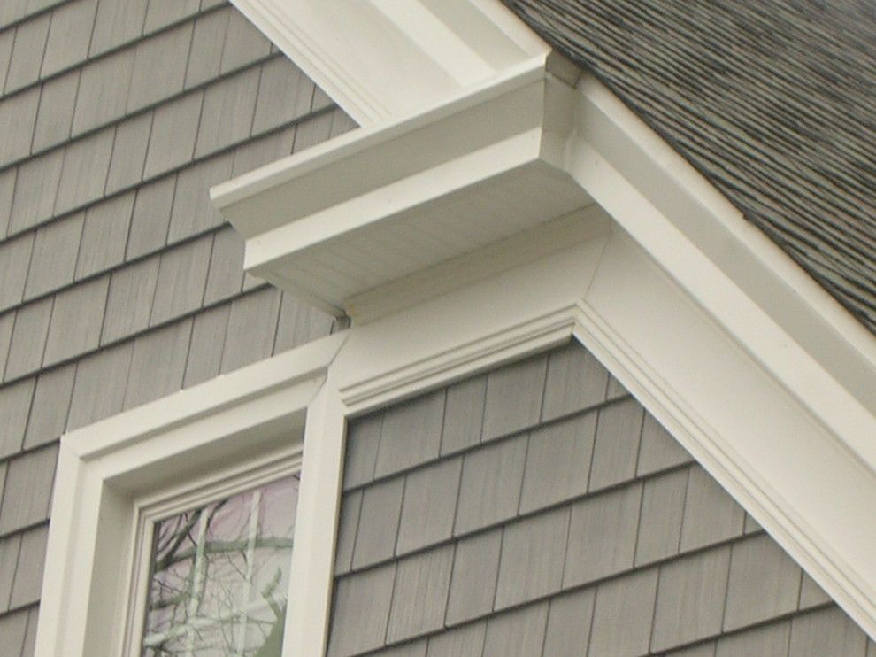 Close-up of a house exterior showing white trim around a window and roofline against gray shingle siding.