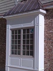 Bay window with white trim and dark roof on a brick building.