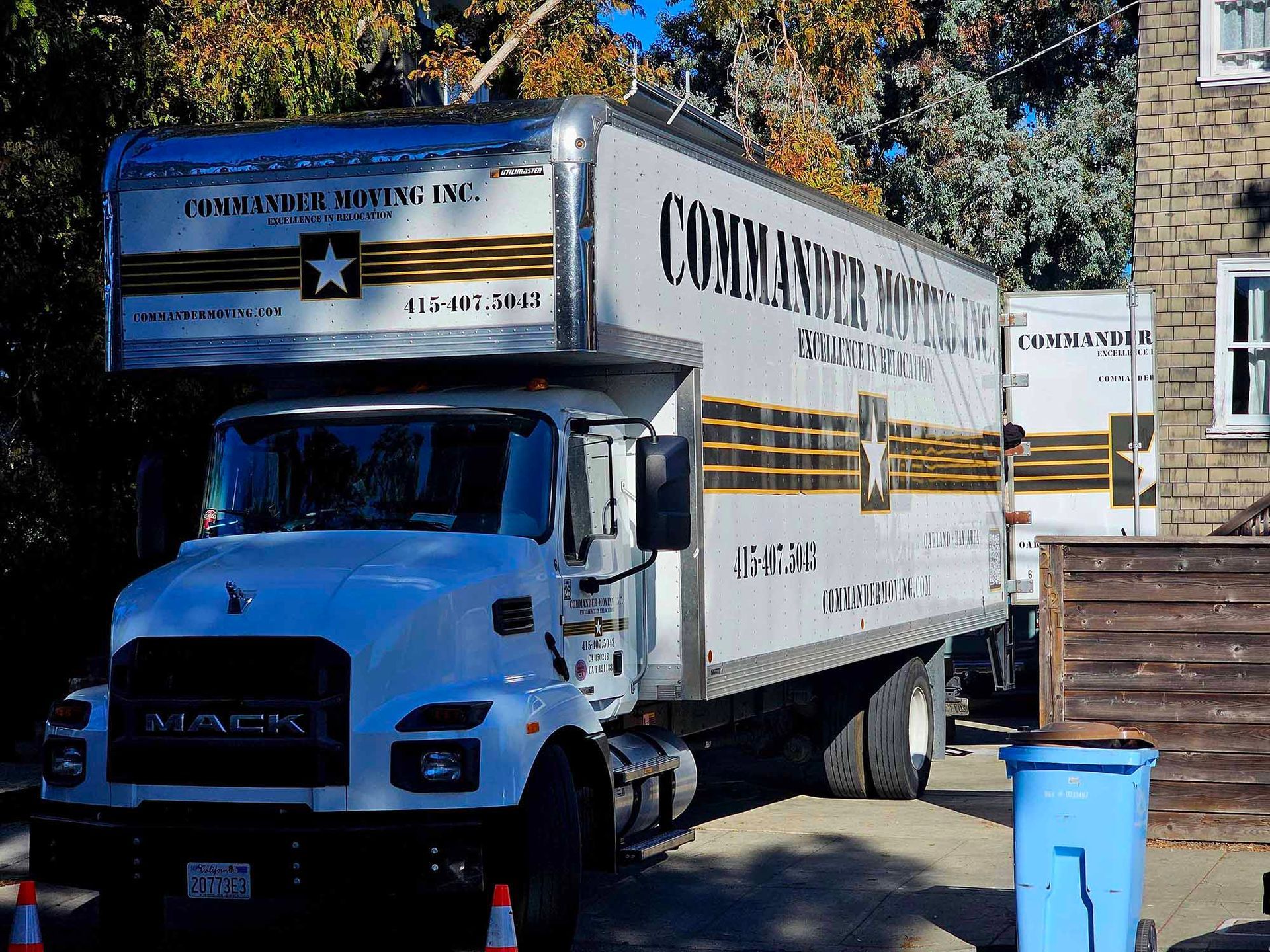 White Commander Motors moving truck parked on a street; a second truck is behind it.