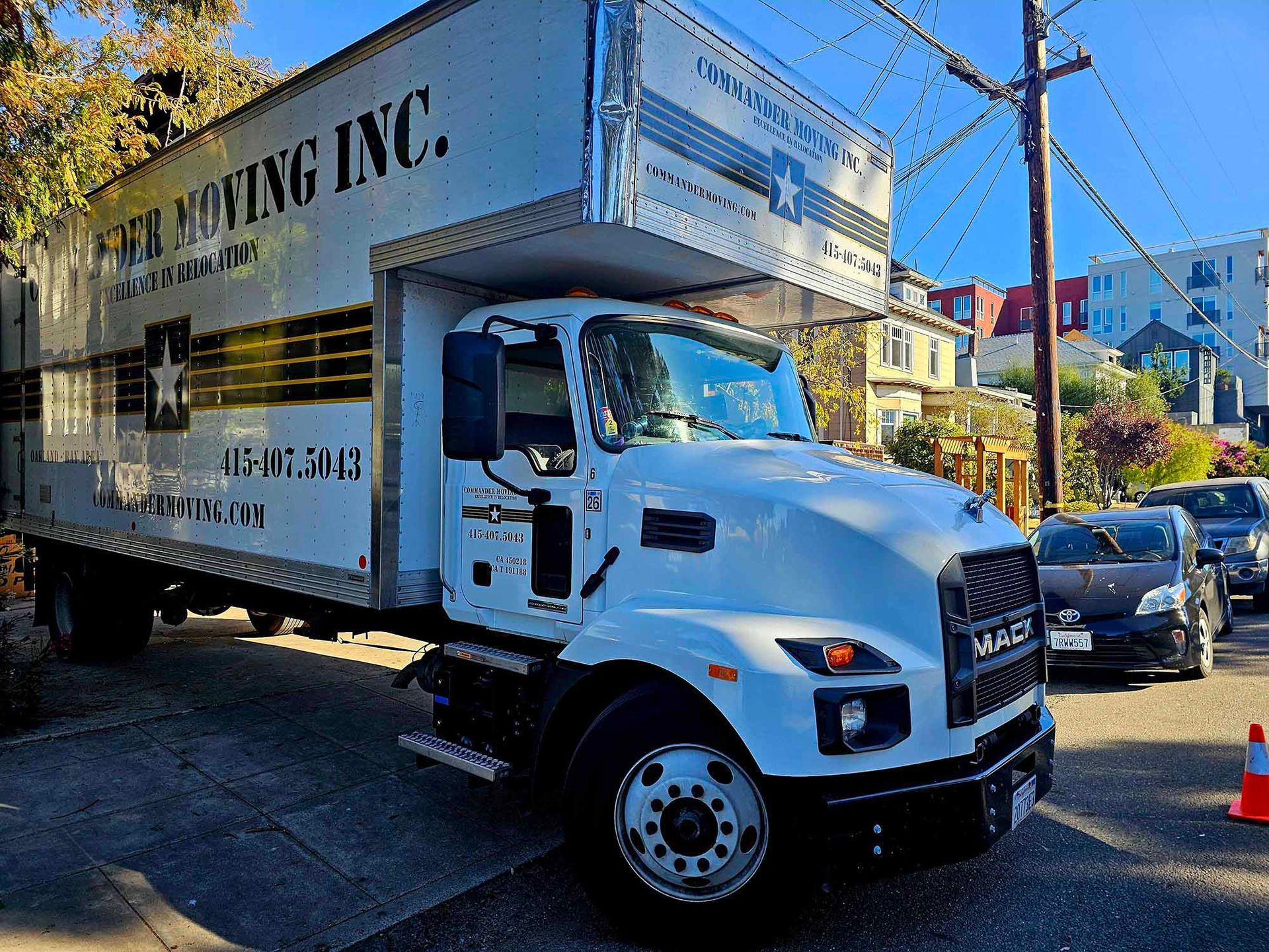 White moving truck parked on a residential street. Truck has company logo and a moving van.