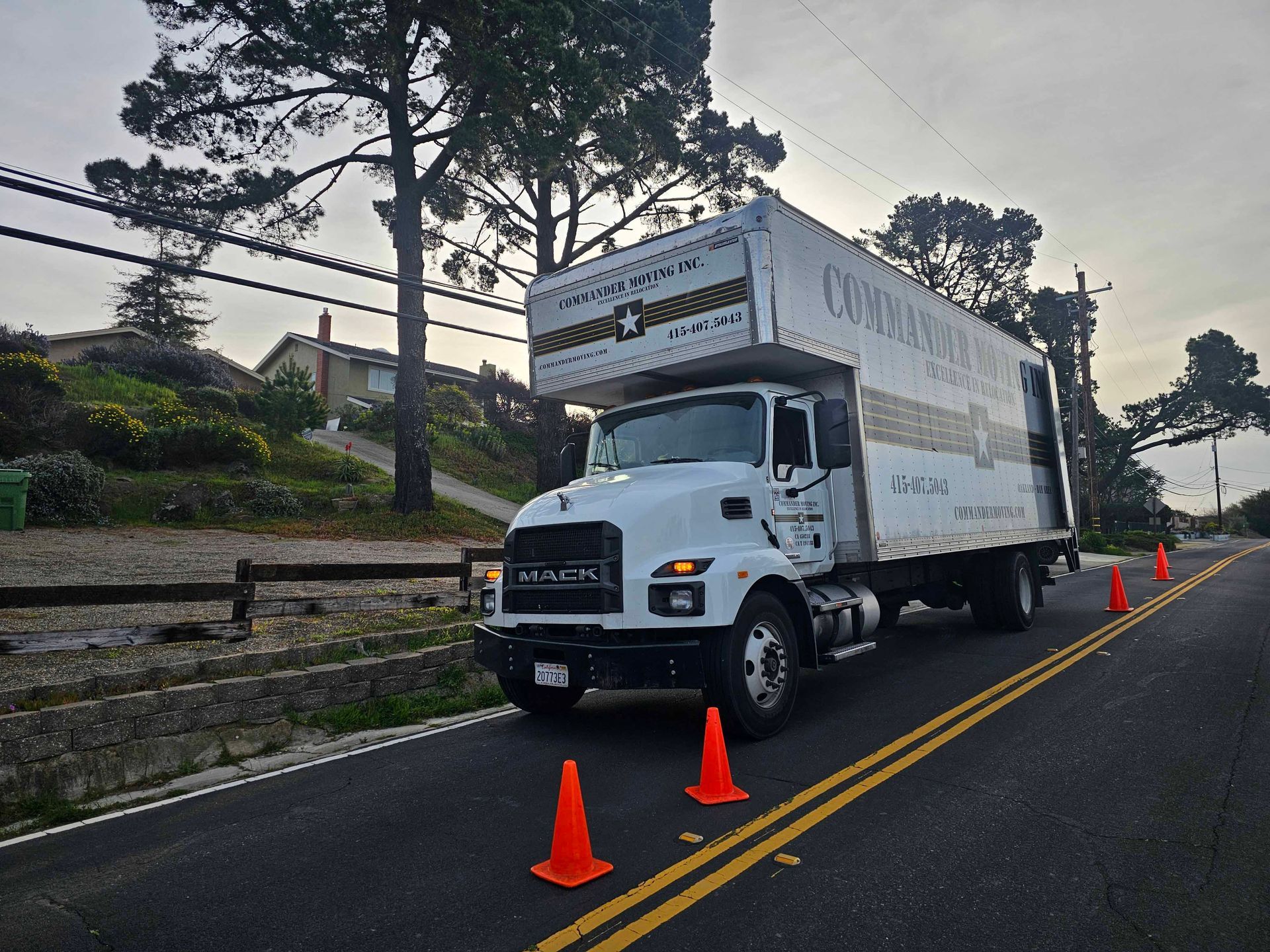 White moving truck parked on a road with orange cones, residential neighborhood background.