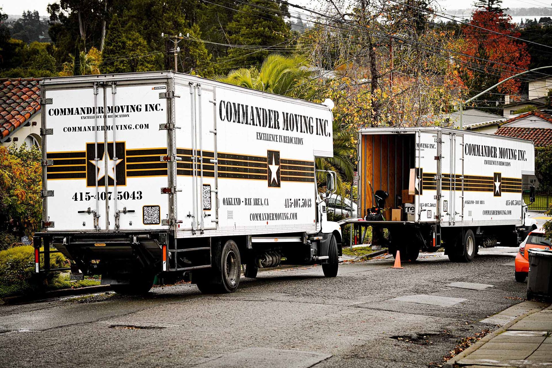 Two white moving trucks parked on a residential street, loading/unloading.