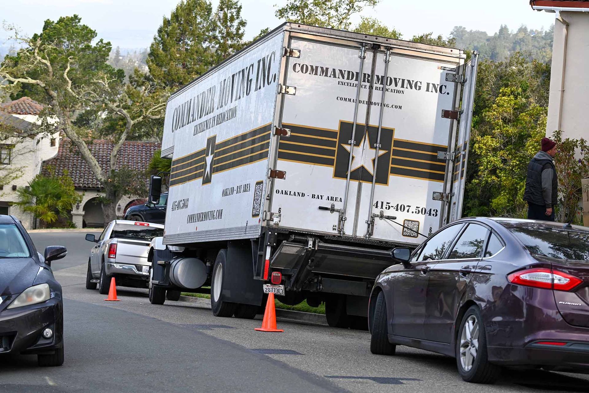 A semi-truck tilted on a street, blocked by cars and traffic cones.