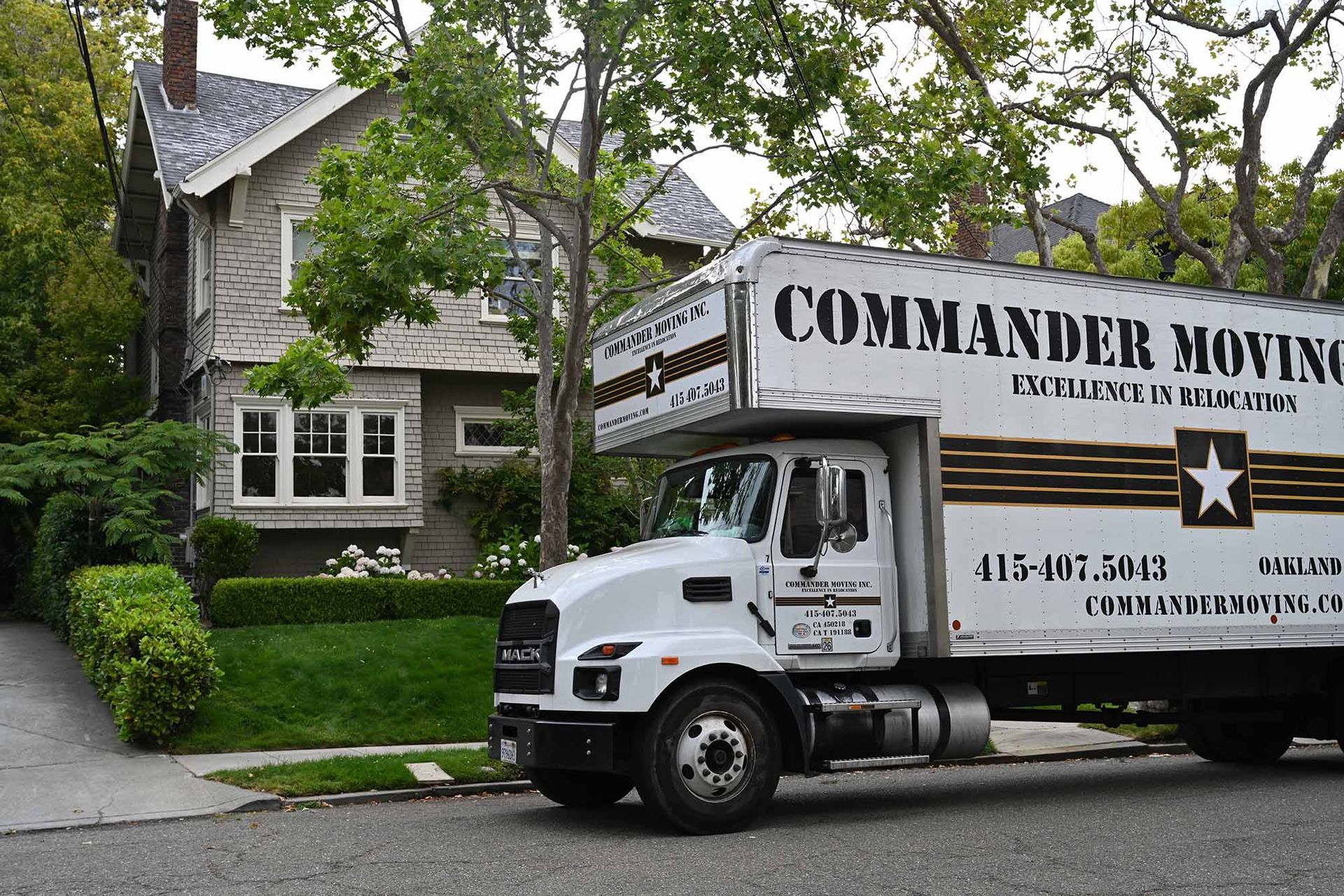 Moving truck parked in front of a house with a Commander Moving logo; trees and bushes are on the sides.