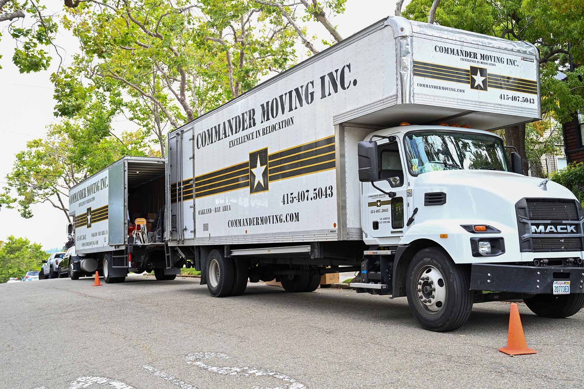 Moving truck on a street, white with black and gold text, unloading items.