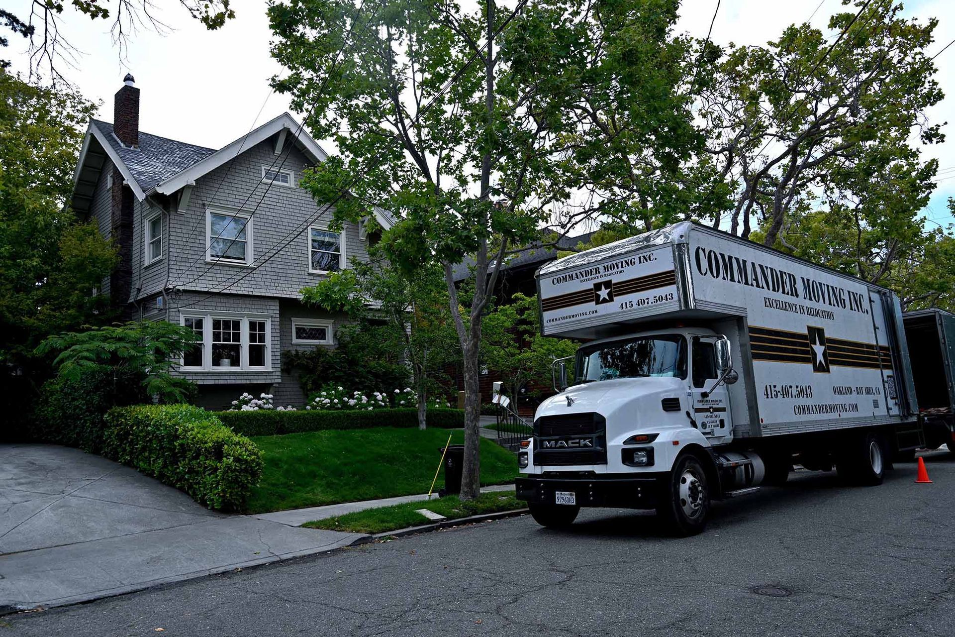 Moving truck parked in front of a two-story grey house with trees.