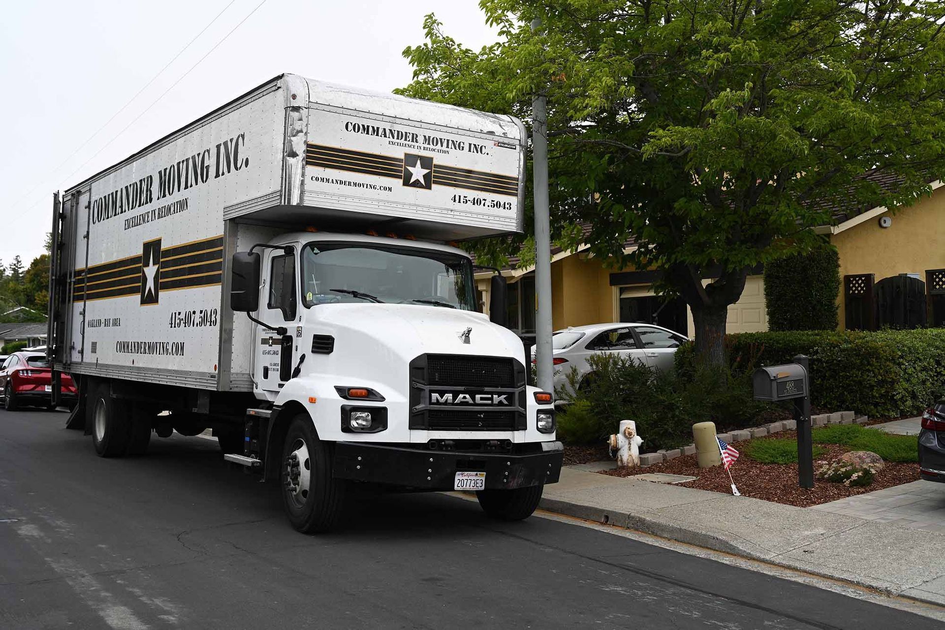 White moving truck parked on residential street, house in the background.