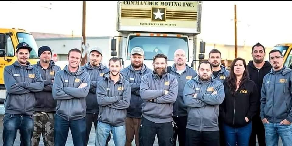 Group of movers posing in front of their truck. Some have crossed arms, all wearing the company uniform.