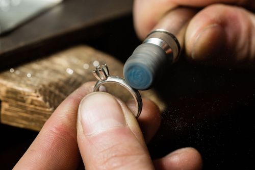 Close-up of hands polishing a silver ring with a rotary tool on a jeweler’s workbench