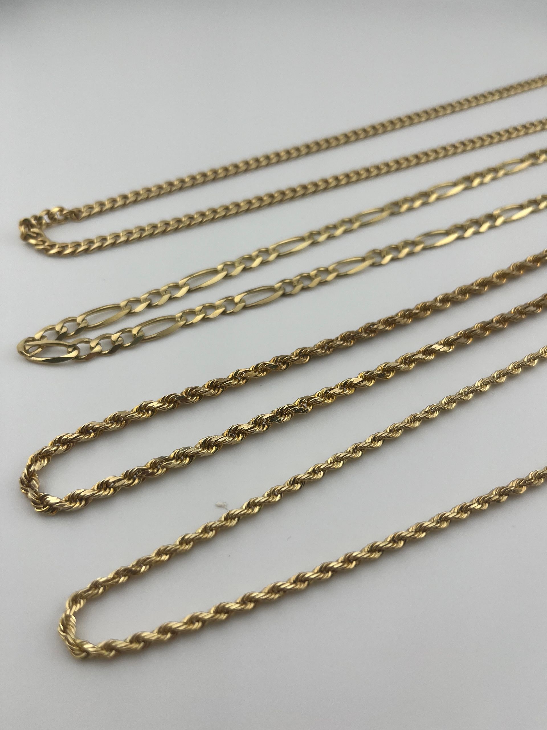 Gold chain necklaces arranged diagonally on a light gray surface.