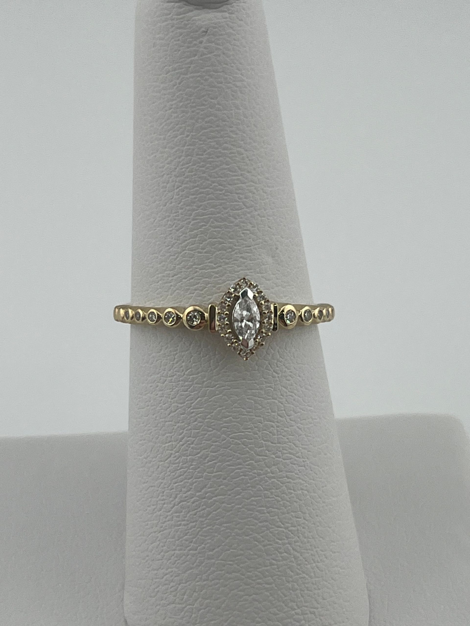 Gold engagement ring with a round center stone on a gray display stand.