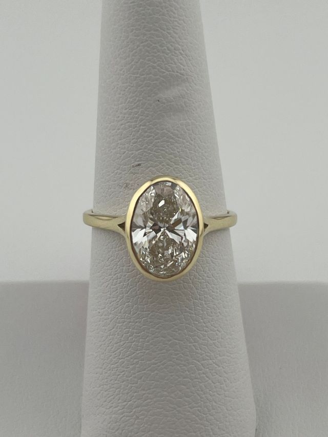 Gold ring with an oval clear gemstone on a gray display cone.
