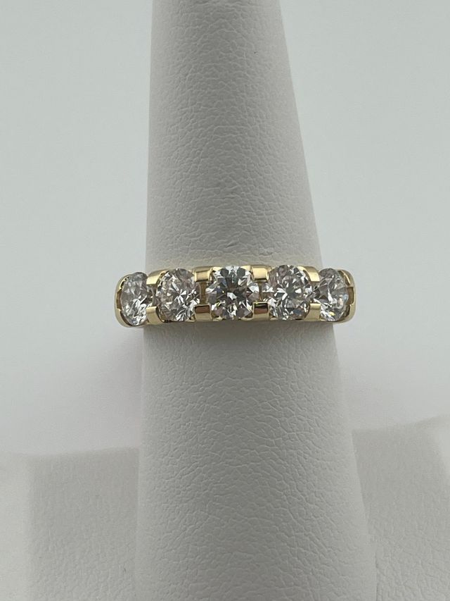 Gold ring with clear gemstones displayed on a gray stand.