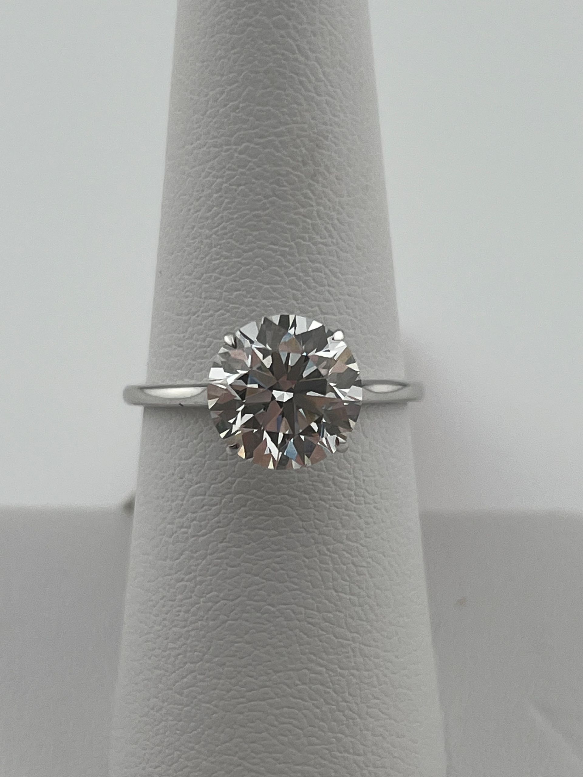 Solitaire diamond ring on a gray display stand.