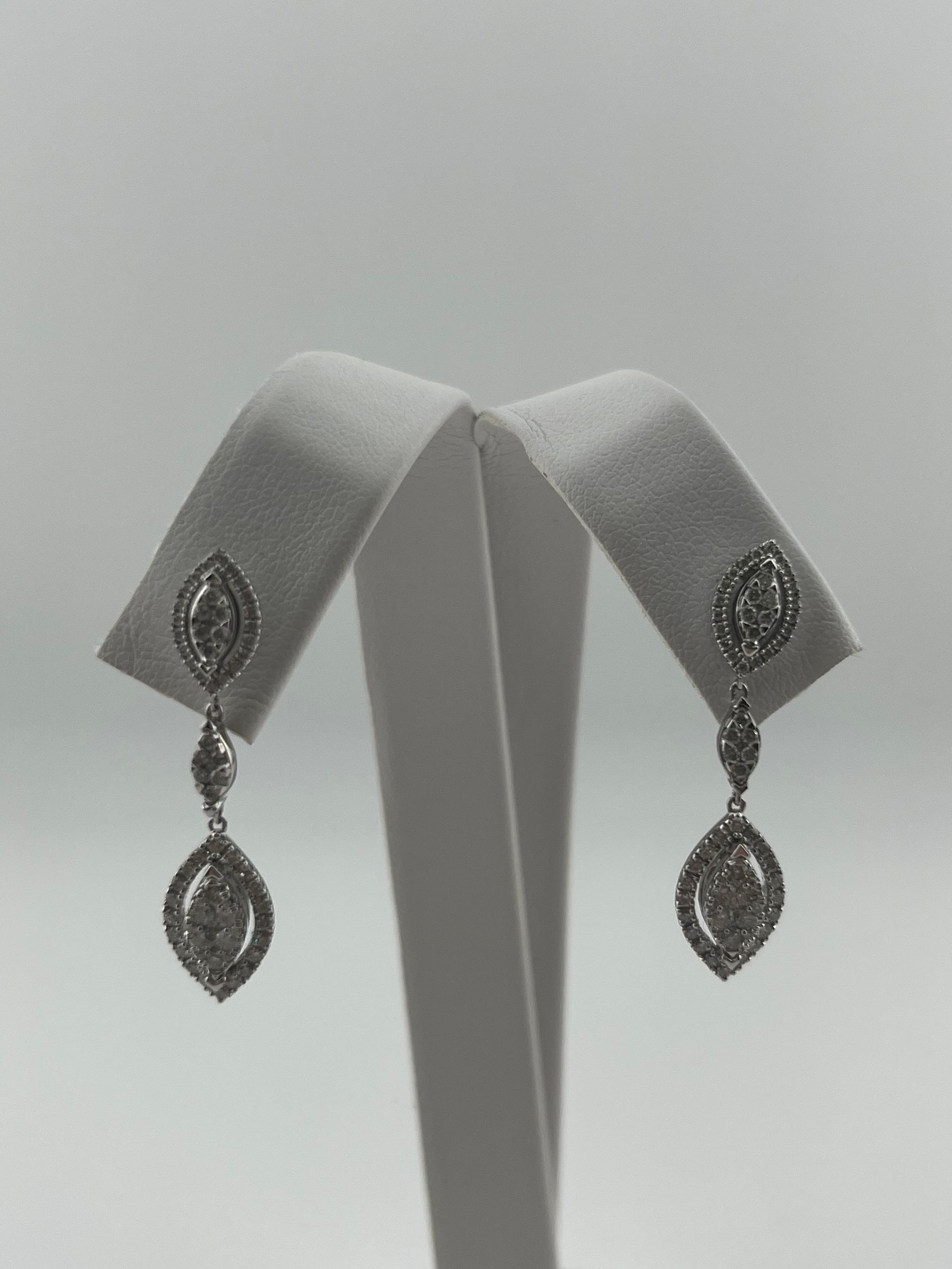 Pair of silver dangling earrings with teardrop designs displayed on a white stand