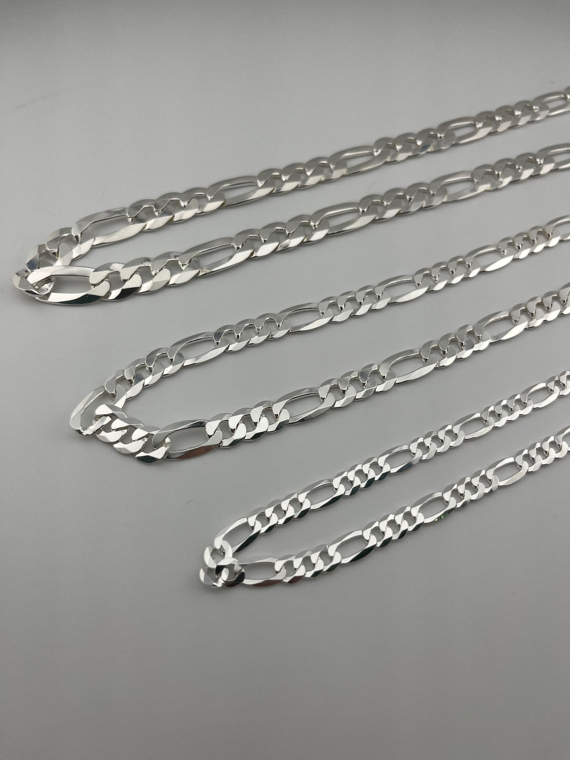 Three silver chain necklaces laid diagonally on a light gray surface.