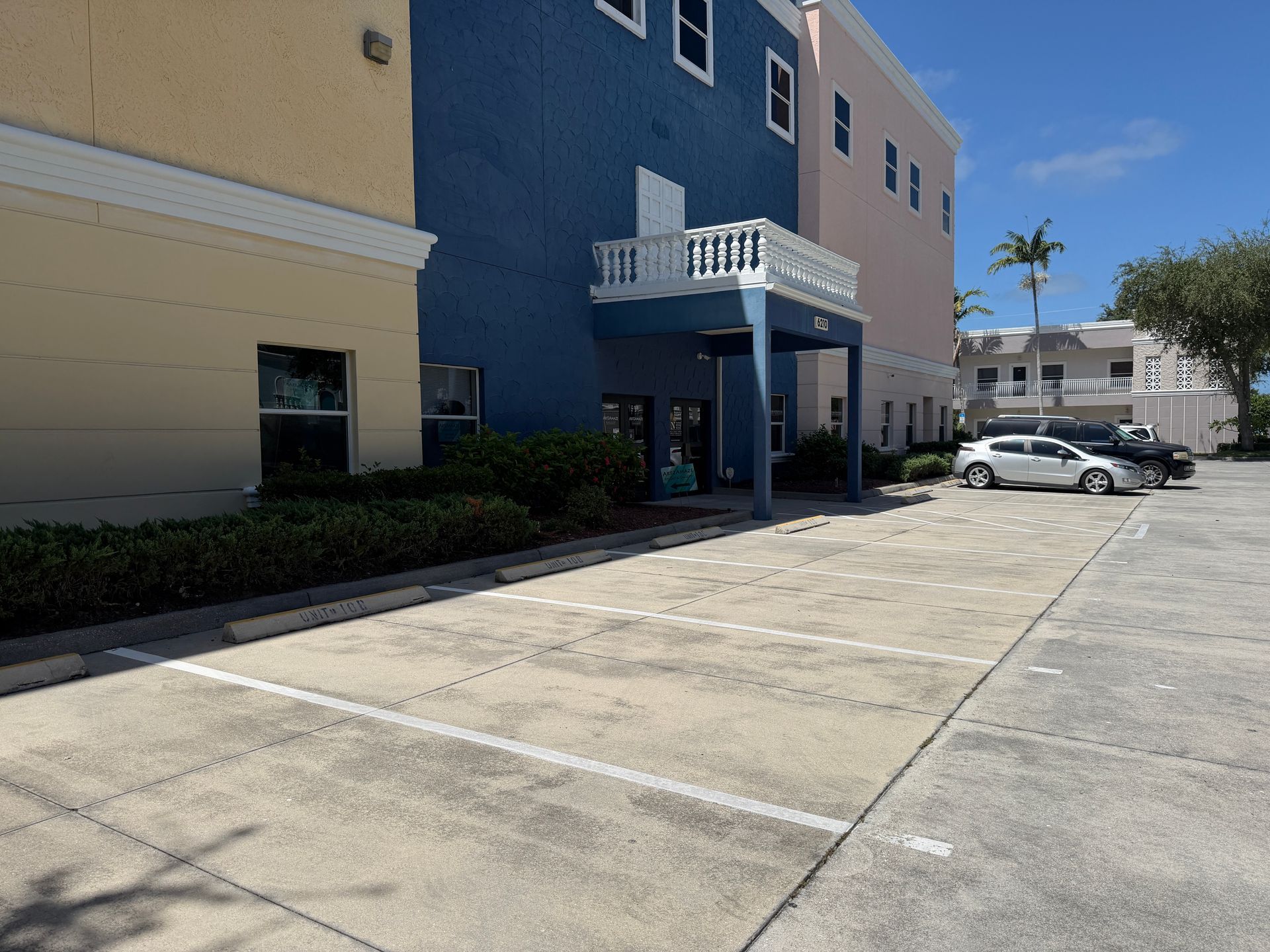 Apartment building entrance with blue awning and parked cars in a sunny lot