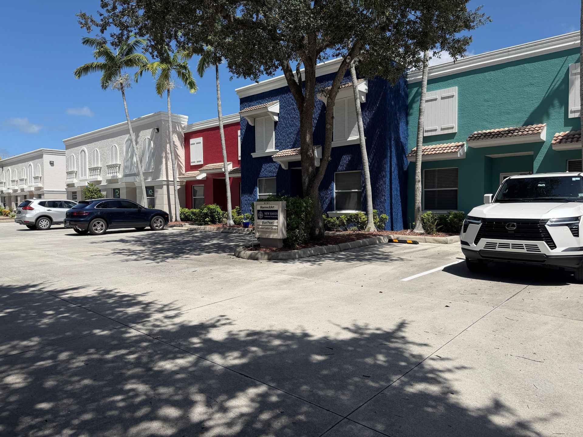 Colorful row of small shops on a sunny street with parked cars and tree shadows