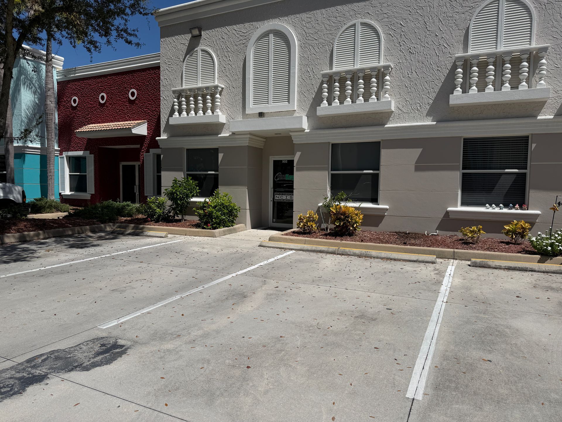 Empty parking lot outside a stucco building with white arched windows and small balconies