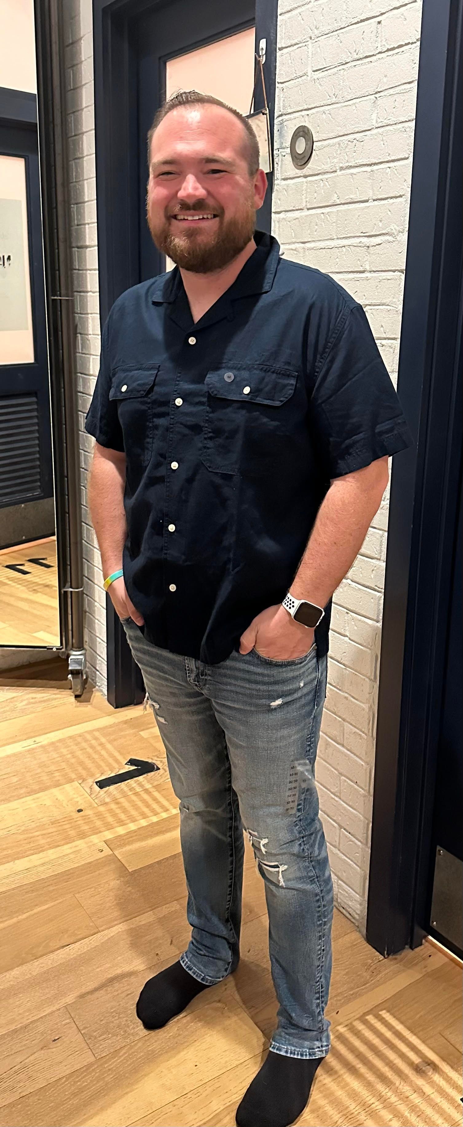 A man with a beard is standing in a dressing room with his hands in his pockets.