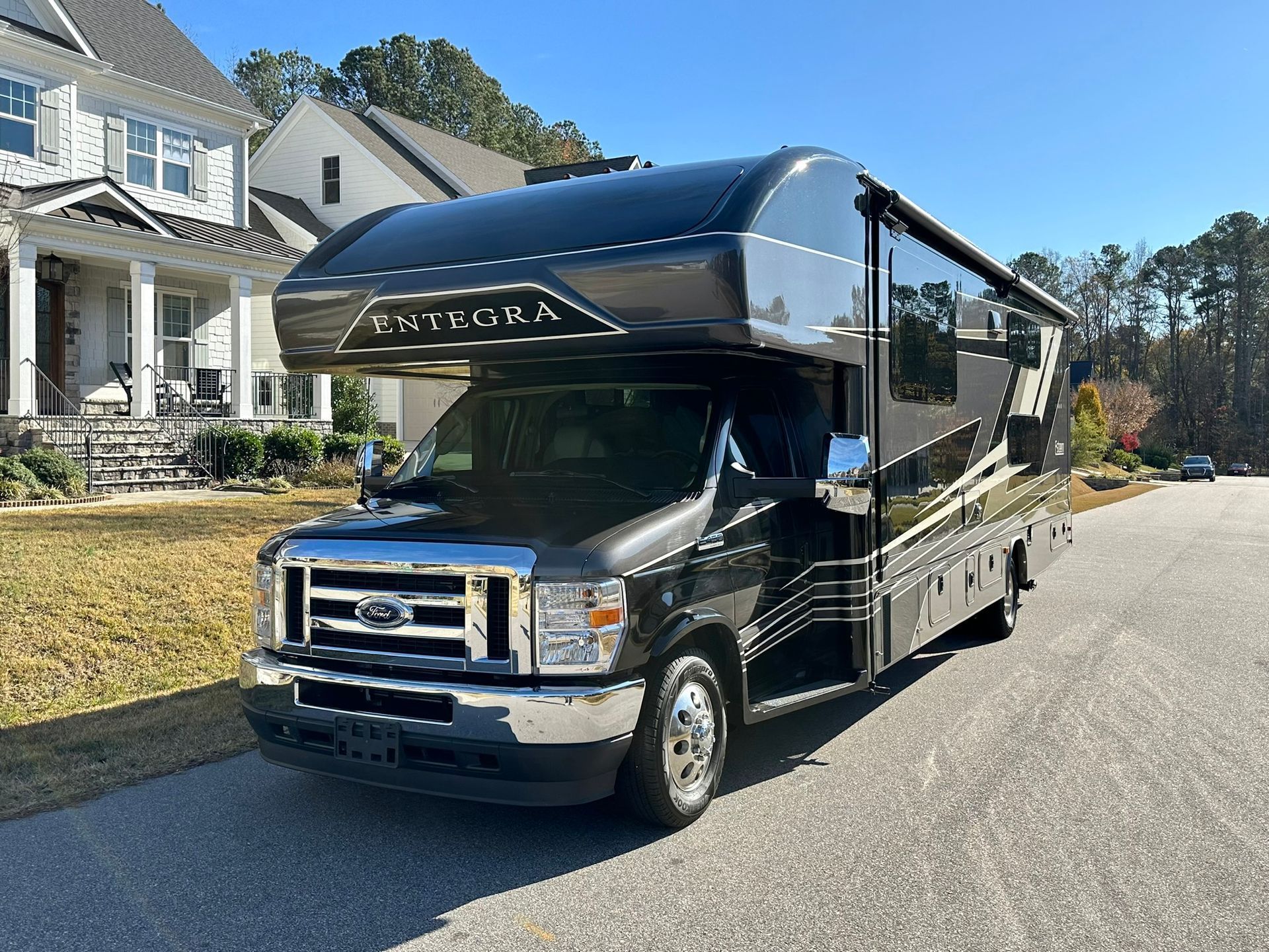 A black rv is parked on the side of the road in front of a house.