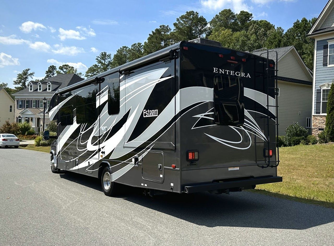 A large rv is parked on the side of the road in front of a house.