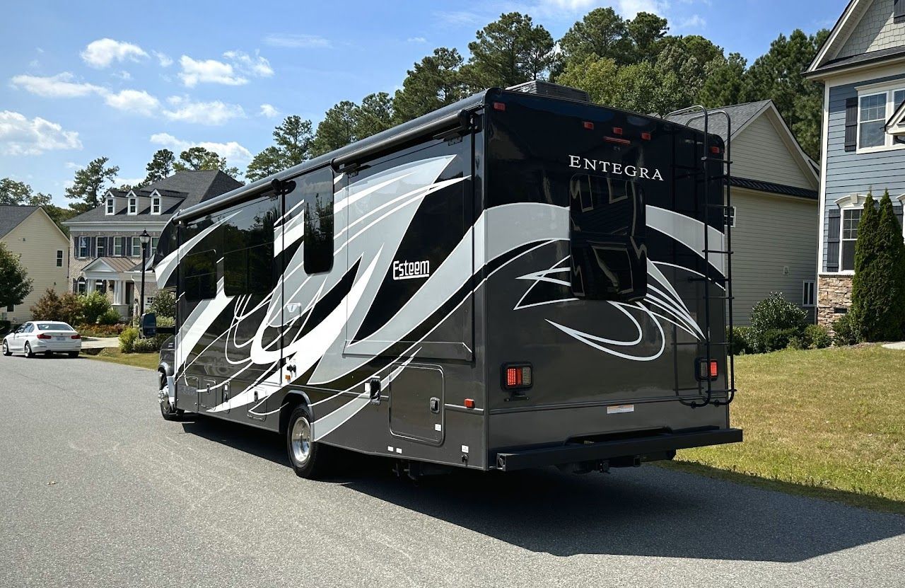 A large rv is parked on the side of the road in front of a house.