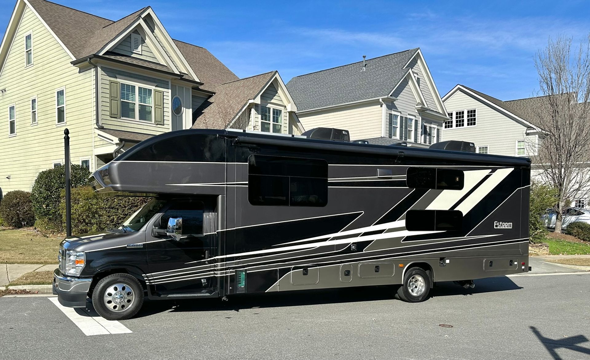 A black and white rv is parked in front of a house.