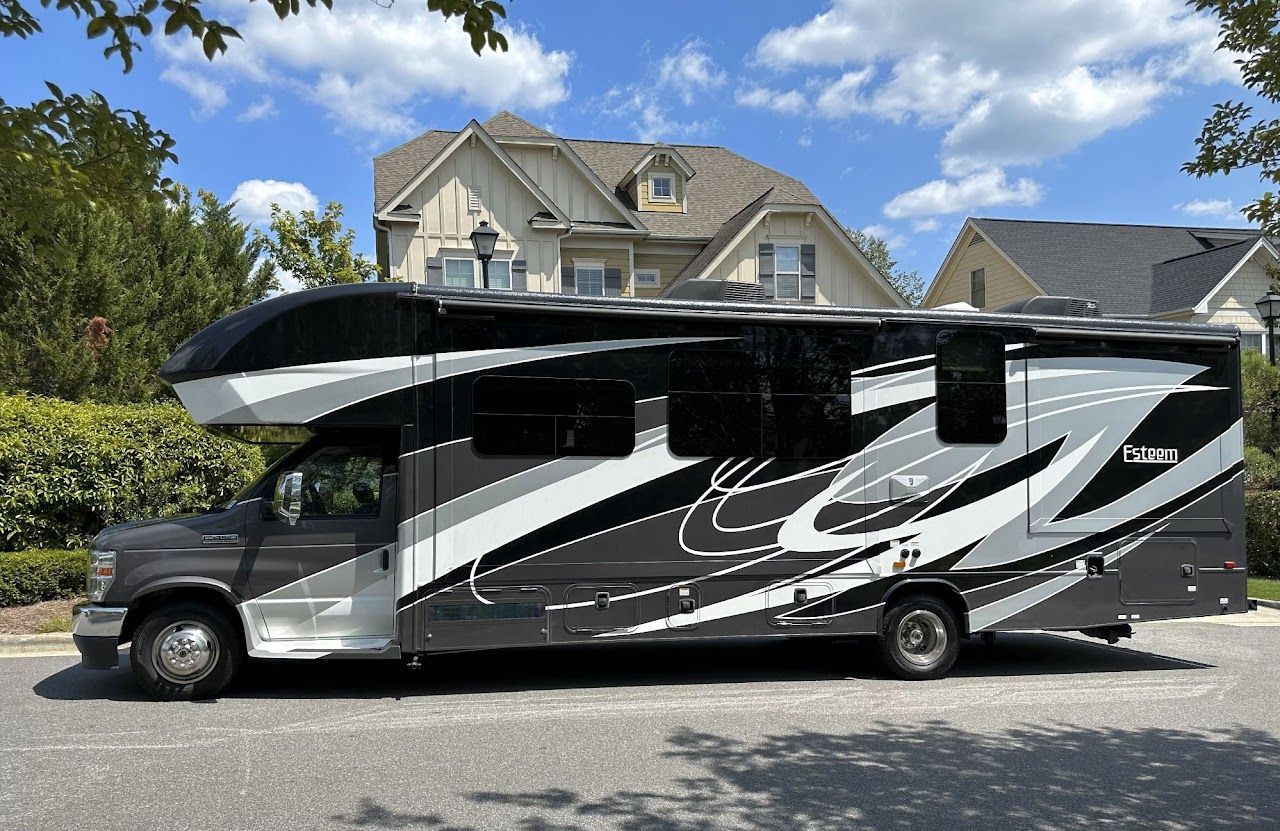 A large black and white rv is parked in front of a house.