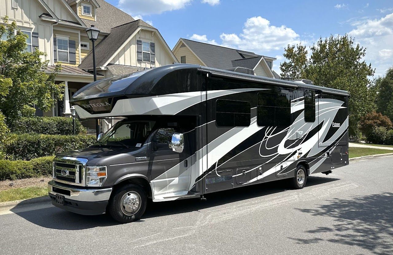 A large black and white rv is parked on the side of the road in front of a house.