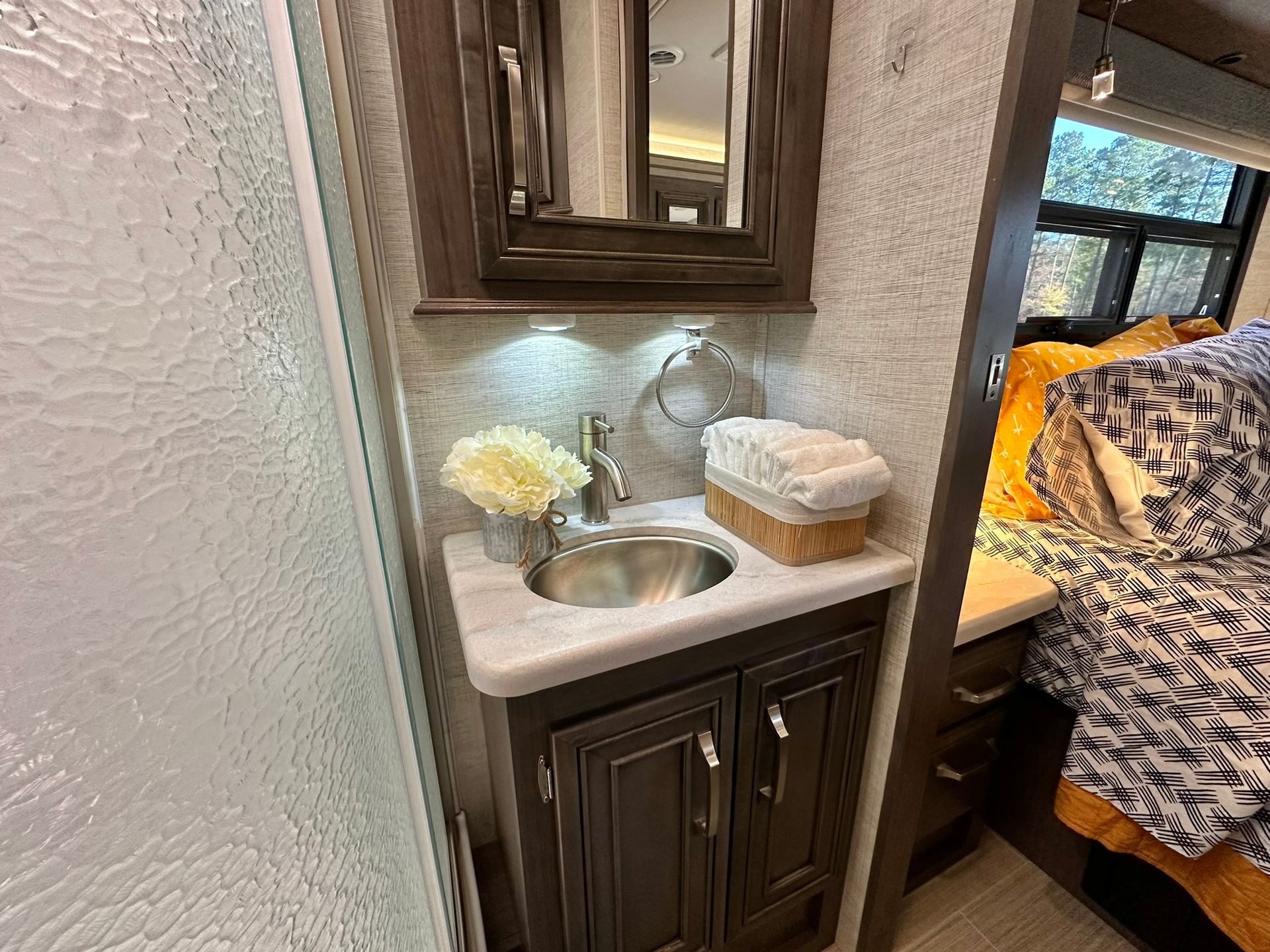 A bathroom in a rv with a sink , mirror and towels.