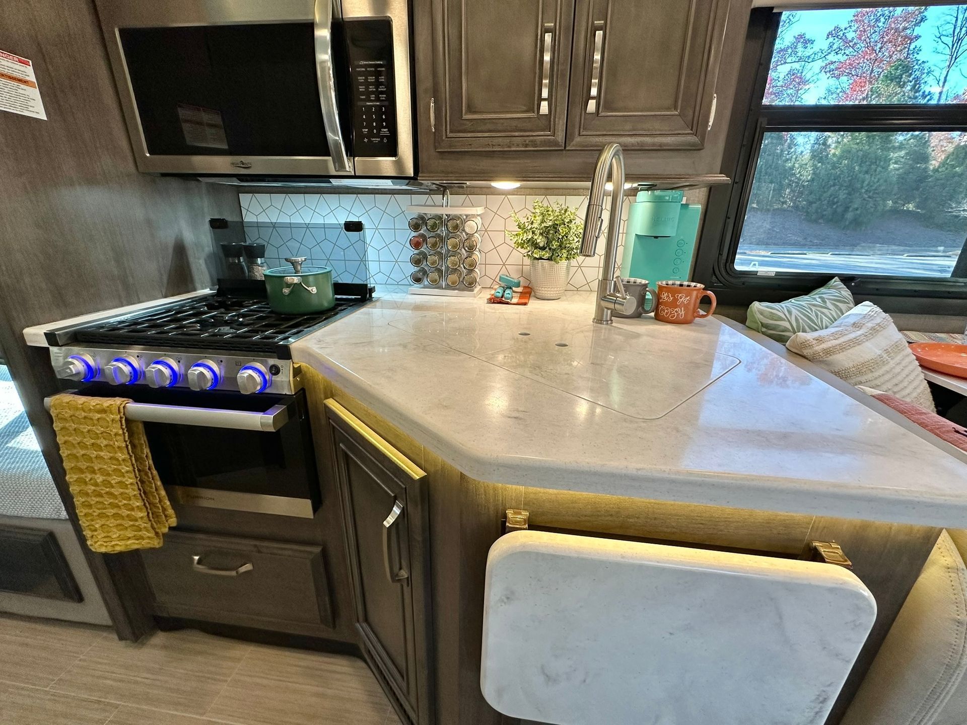 A kitchen in a rv with a stove , microwave and sink.
