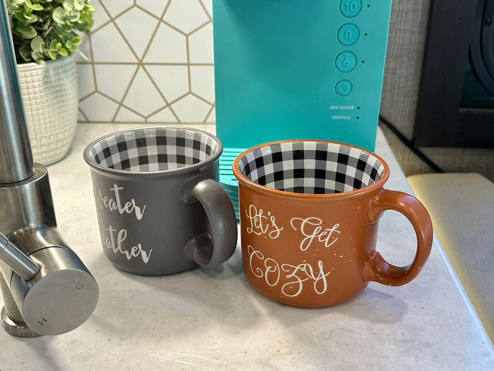 Two coffee mugs are sitting on a counter next to a coffee maker.