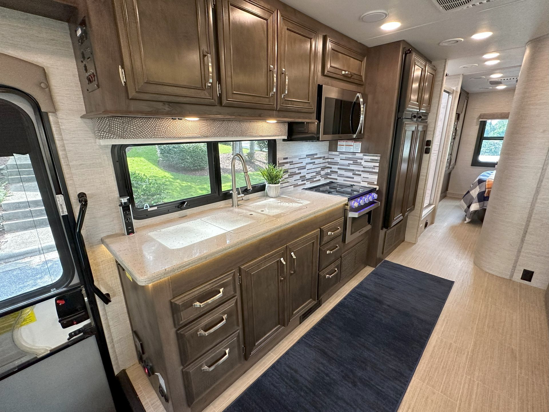 A kitchen in a rv with a sink , stove , microwave and refrigerator.