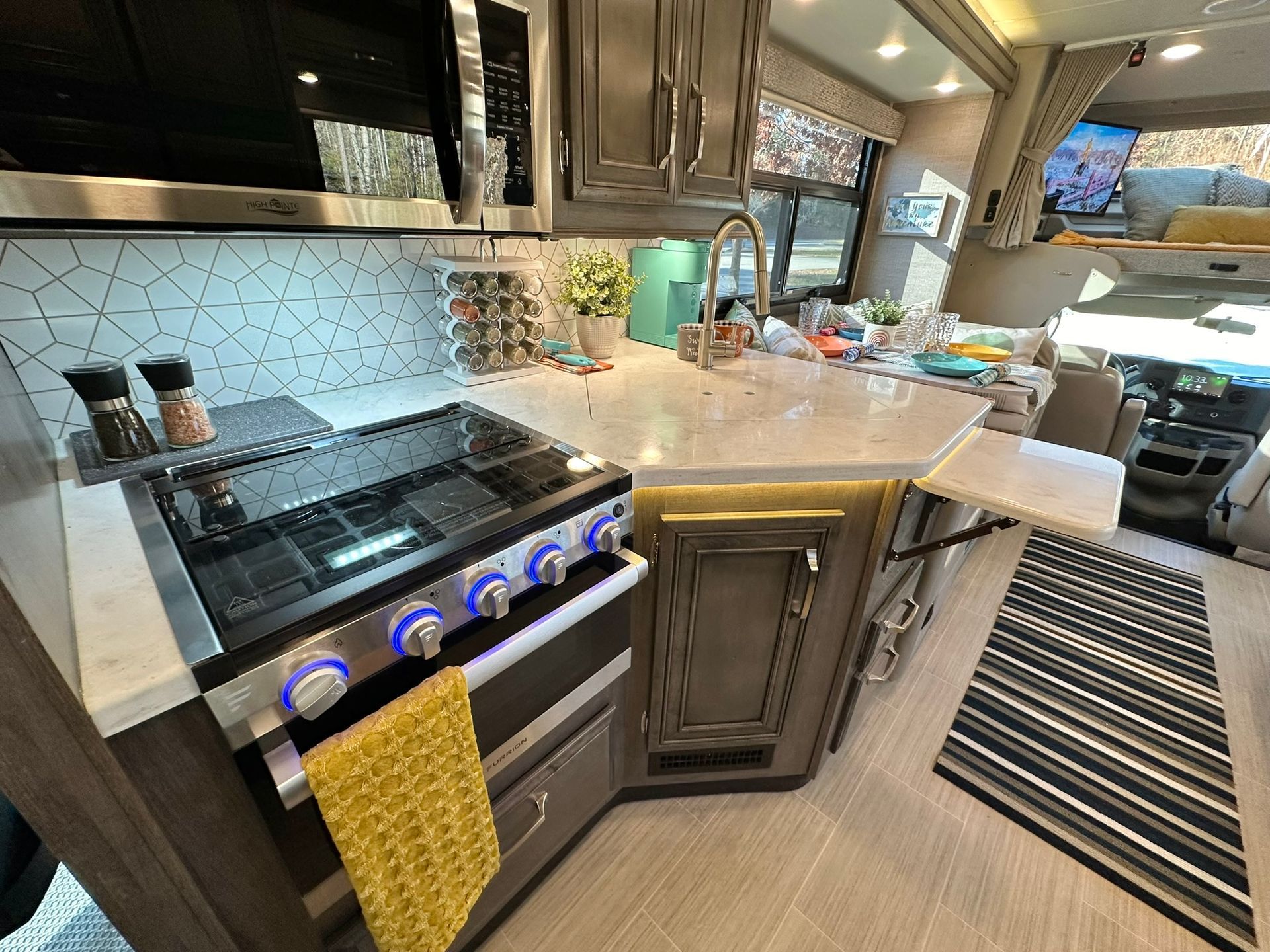 A kitchen in a rv with a stove , sink , and microwave.